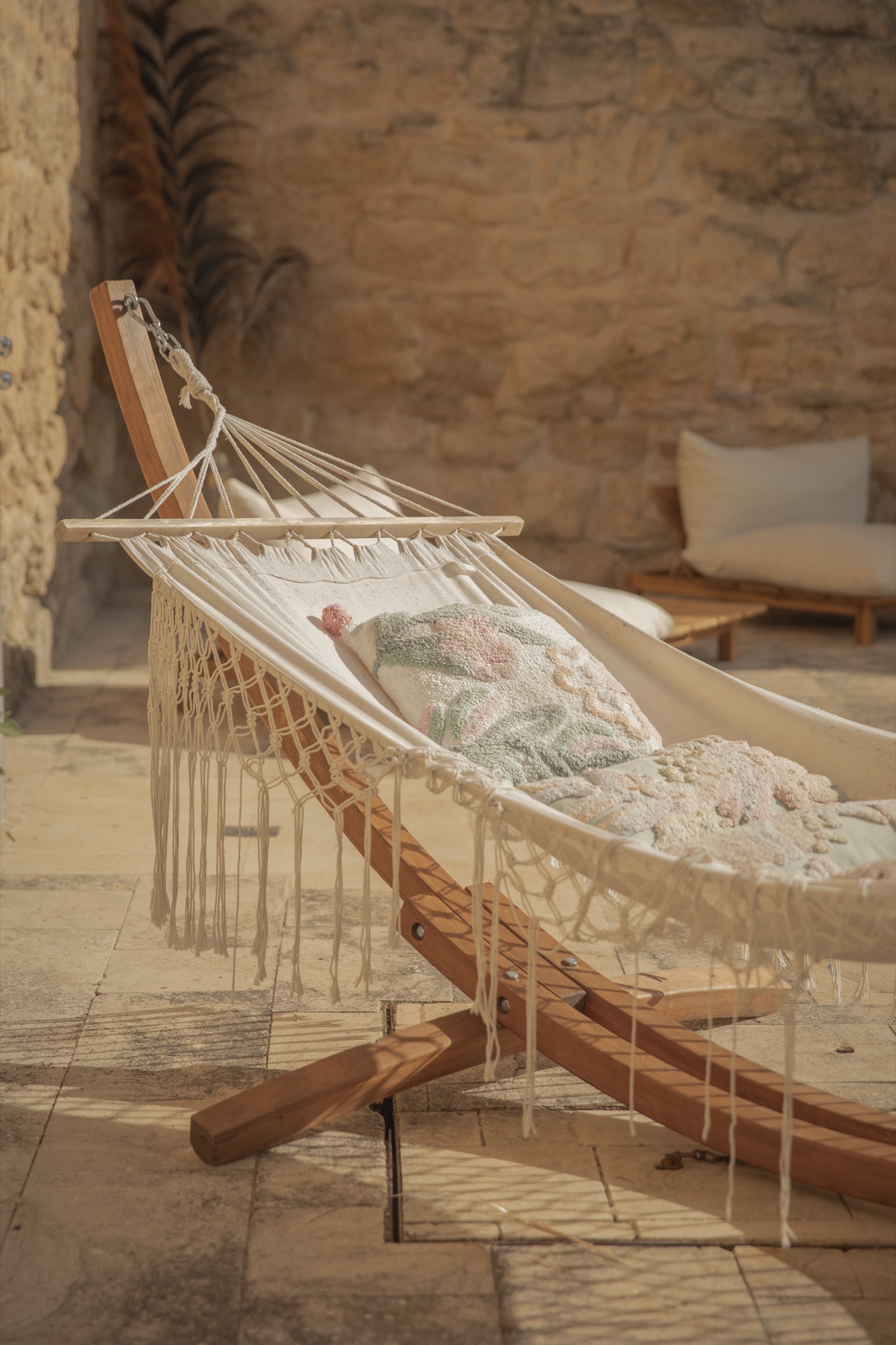 A hammock with embroidered cushions in a stone-walled courtyard, afternoon light