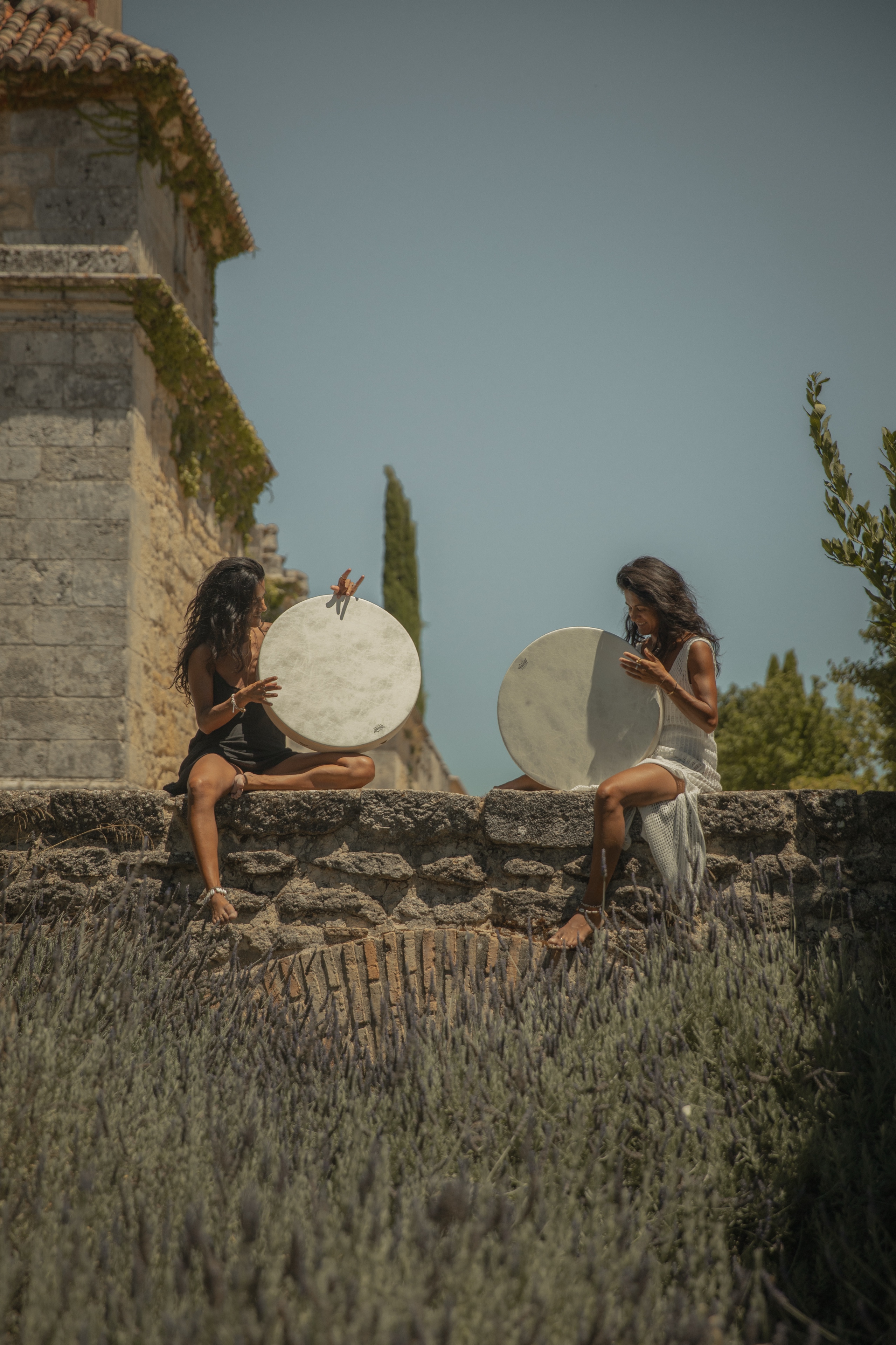 Two practitioners with frame drums on a stone wall